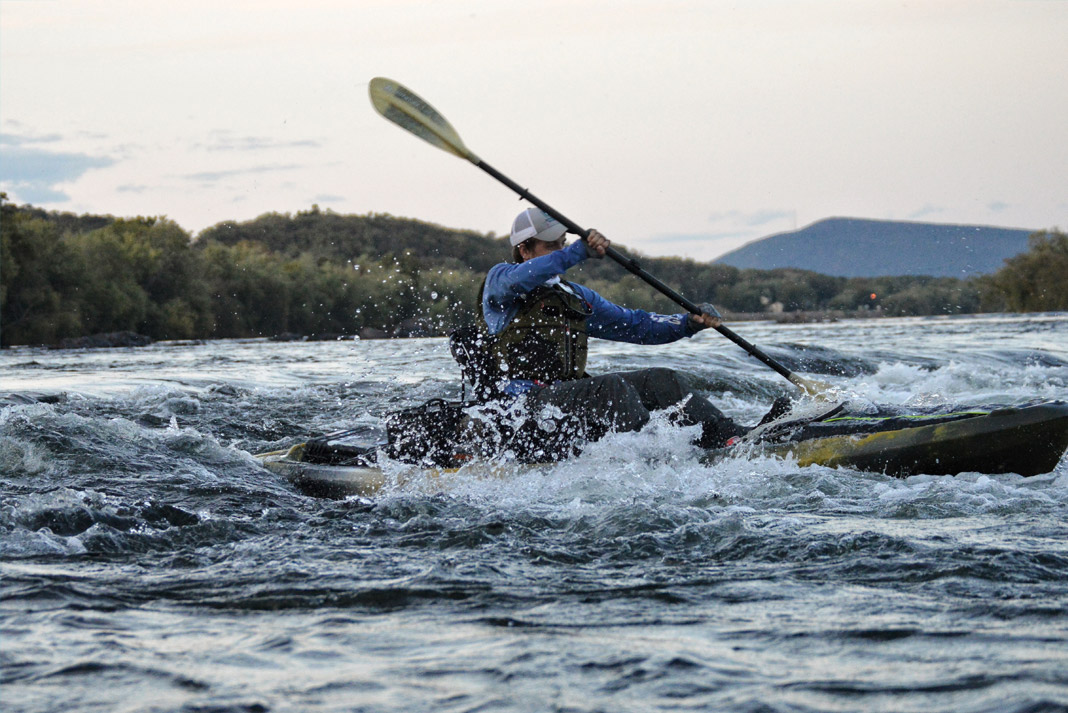 A kayak angler runs through a fast moving river.