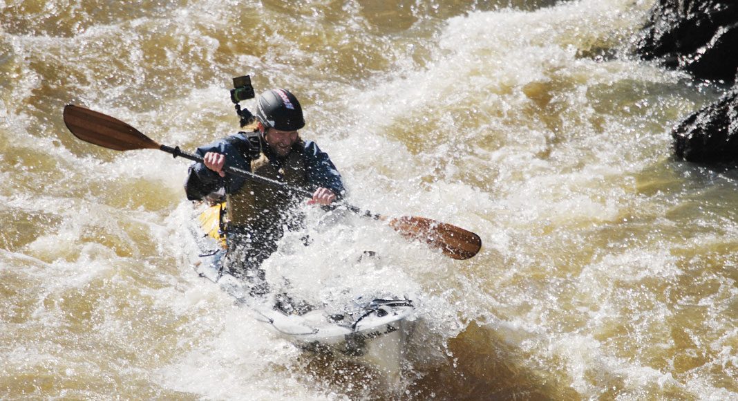 A kayak angler paddles into a big rapid.
