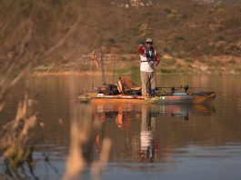 man stands and fishes from an Old Town kayak while wearing an inflatable life jacket
